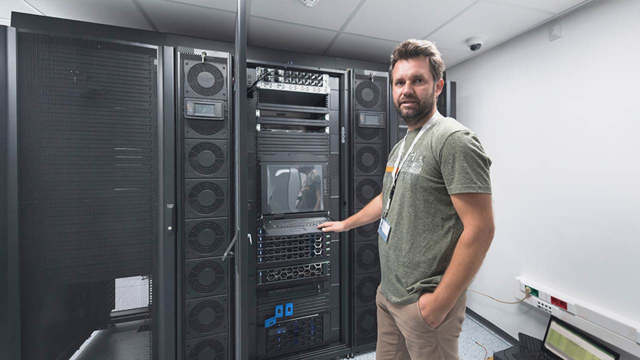 IT technician standing in a secure server room with open rack-mounted equipment, representing Piccola Tech’s professional IT support services.