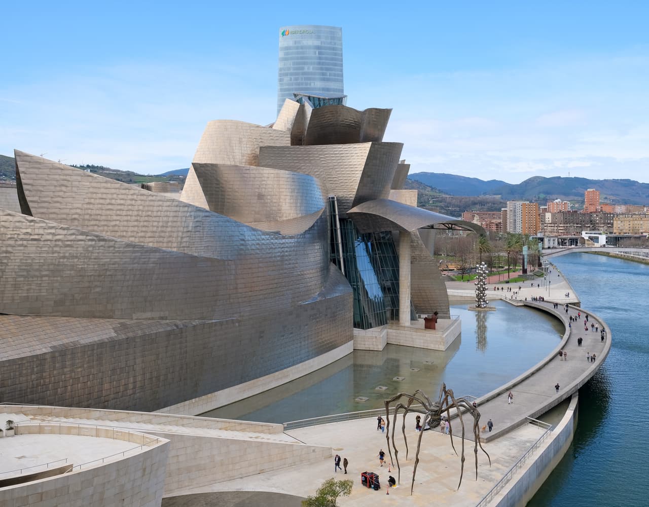 Guggenheim Museum Bilbao viewed from the northwest, with sculptural titanium forms reflecting light beside the Nervión River.