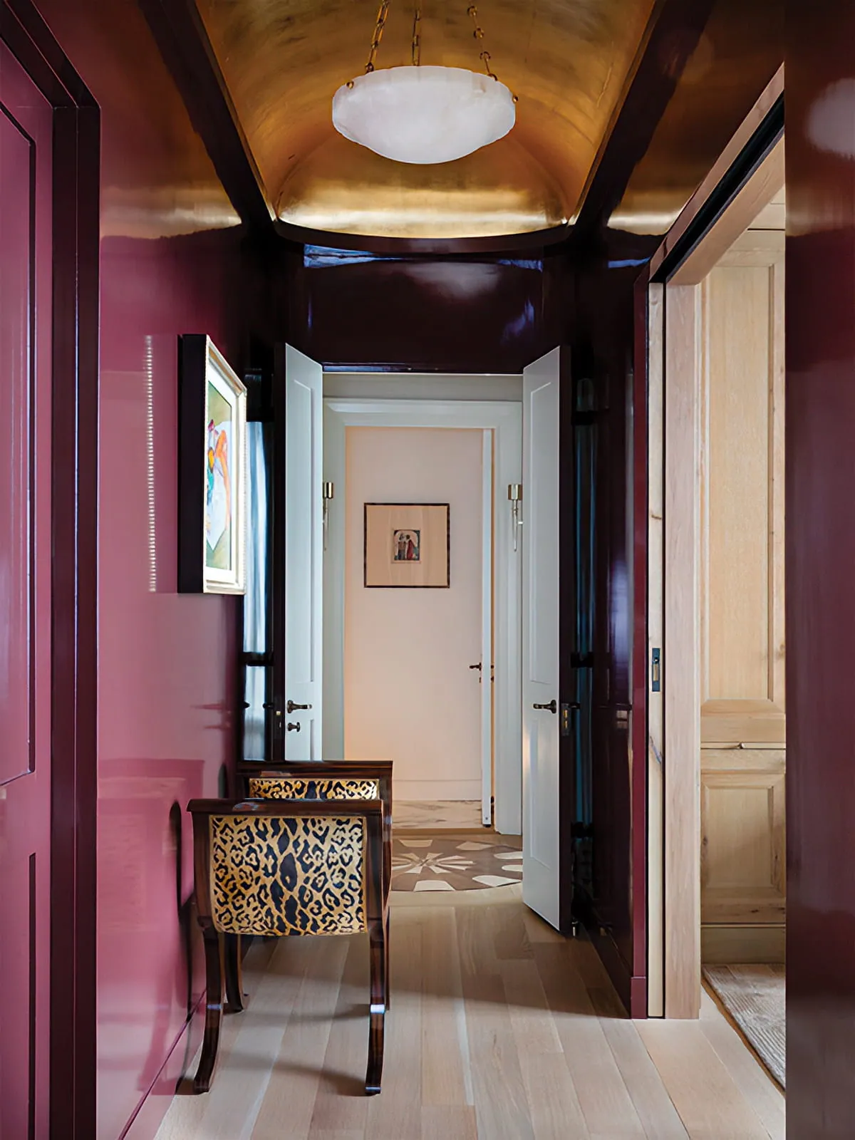 Burgundy hallway with dark wood ceiling beams, paneled doorways, geometric flooring, and sculptural lighting.