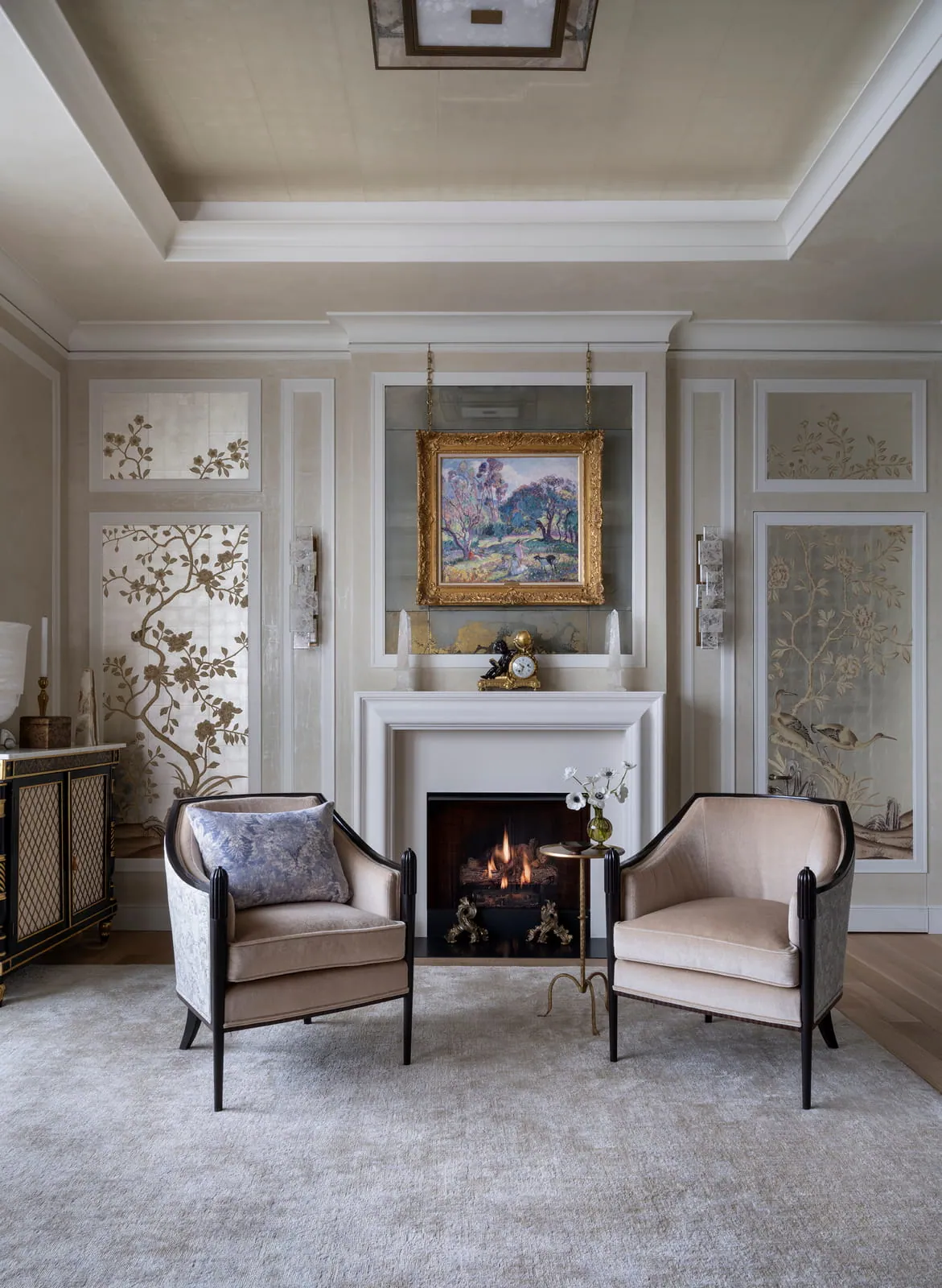 Paneled sitting area with a marble fireplace, paired armchairs, framed artwork, and decorative glass doors.