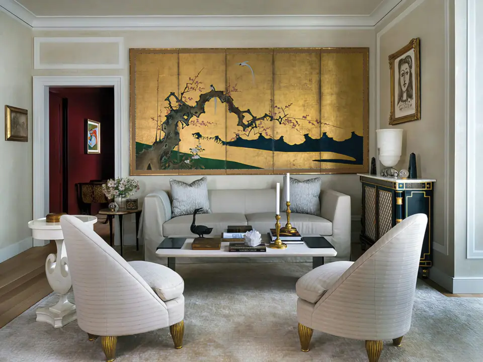 Formal living room with classical wall paneling, curved chairs, and a gold decorative screen behind the sofa.