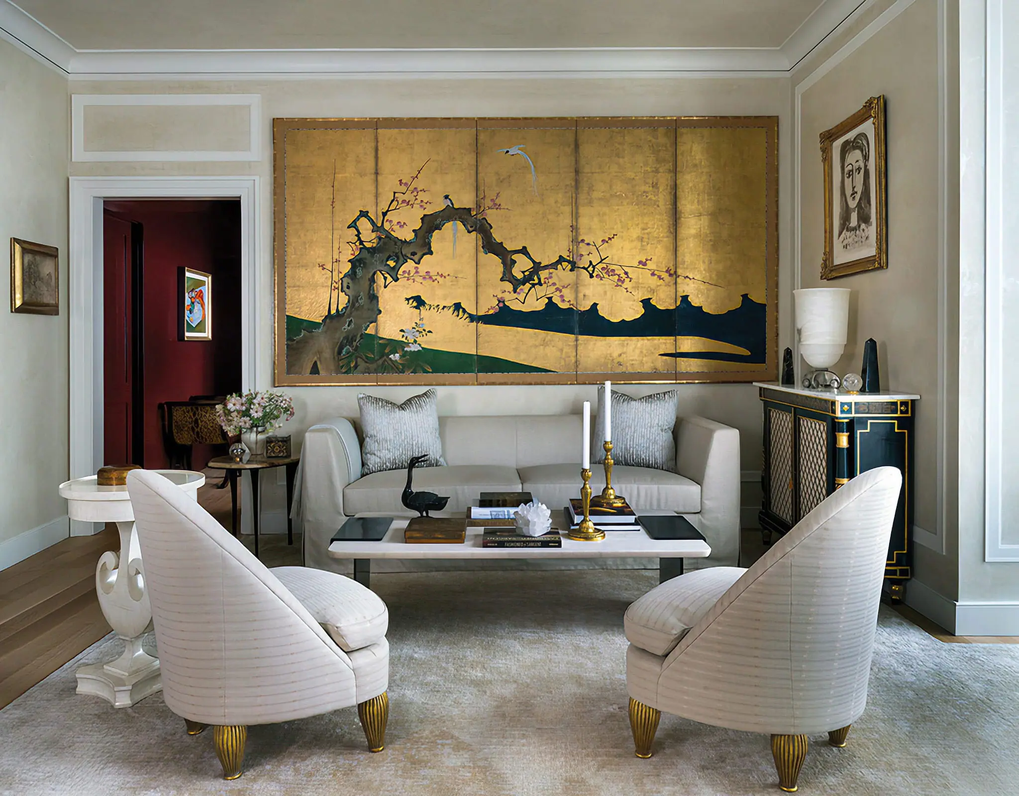 Formal living room with classical wall paneling, curved chairs, and a gold decorative screen behind the sofa.