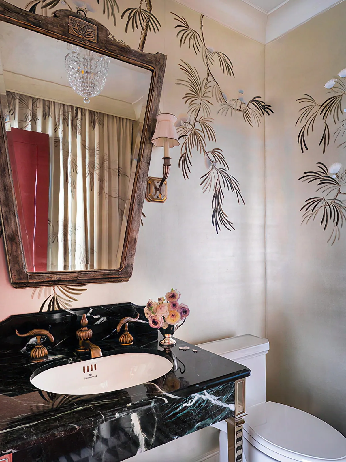 Powder room with botanical wallpaper, black marble vanity, sculptural mirror, and polished metal fixtures.
